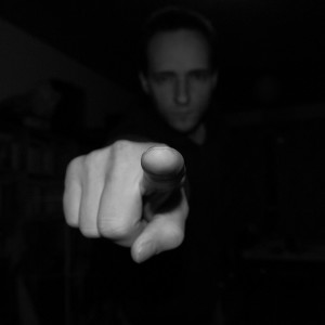 Black and white photograph of a hand with index finger pointing towards the camera; blame.