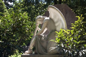 Alabaster statue of an angel at rest, chin in hand, in a garden