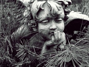 Statue of a cherub, chin in hand, gazing downwards, slight amusement on its face.
