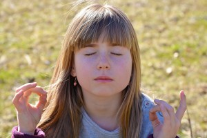 Photo of a 10 year old girl, eyes closed, thumbs joined to forefingers on both hands, meditating.