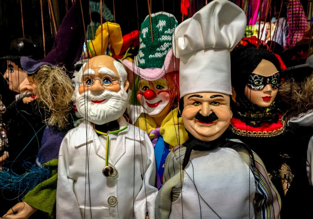 An array of colorful puppets in different guises: a chef, a baker, a masked Venetian dancer.