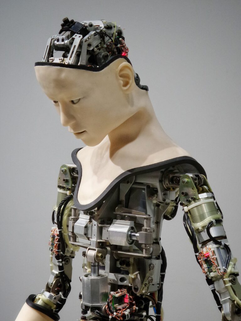 A humanoid robot, skin covering its neck and thoughtful face, but with the top of its head and below its shoulders without skin, so as to expose the machinery beneath.