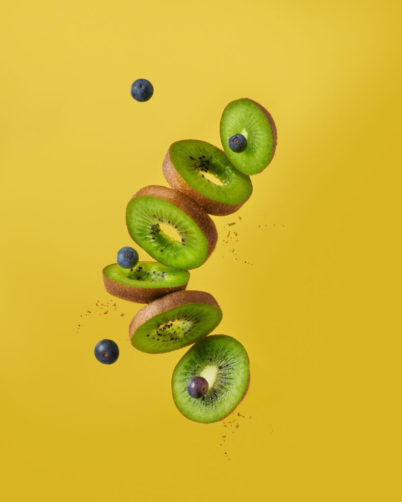 Kiwifruit slices and blueberries in mid air against a gold ground