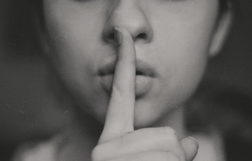 Photograph of a face, below the eyes, with index finger to her lips: shhhh