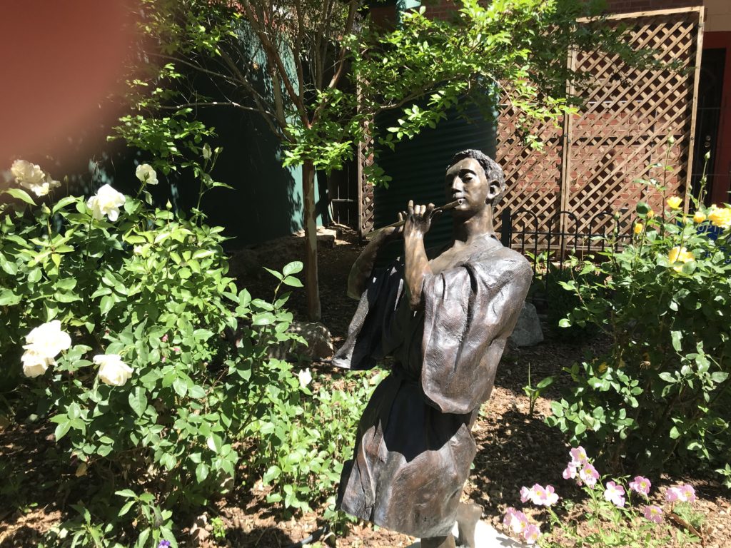Statue of the youth Pan, playing his flute in a garden of roses. Bisbee, AZ 