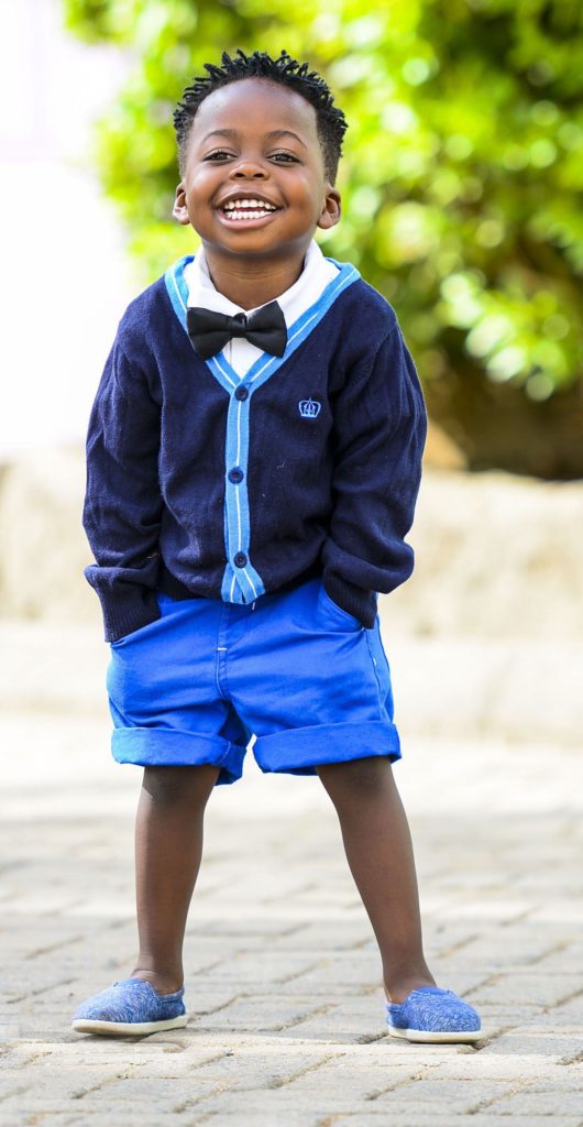Four year old boy in blue shorts, navy cardigan, and bow tie.