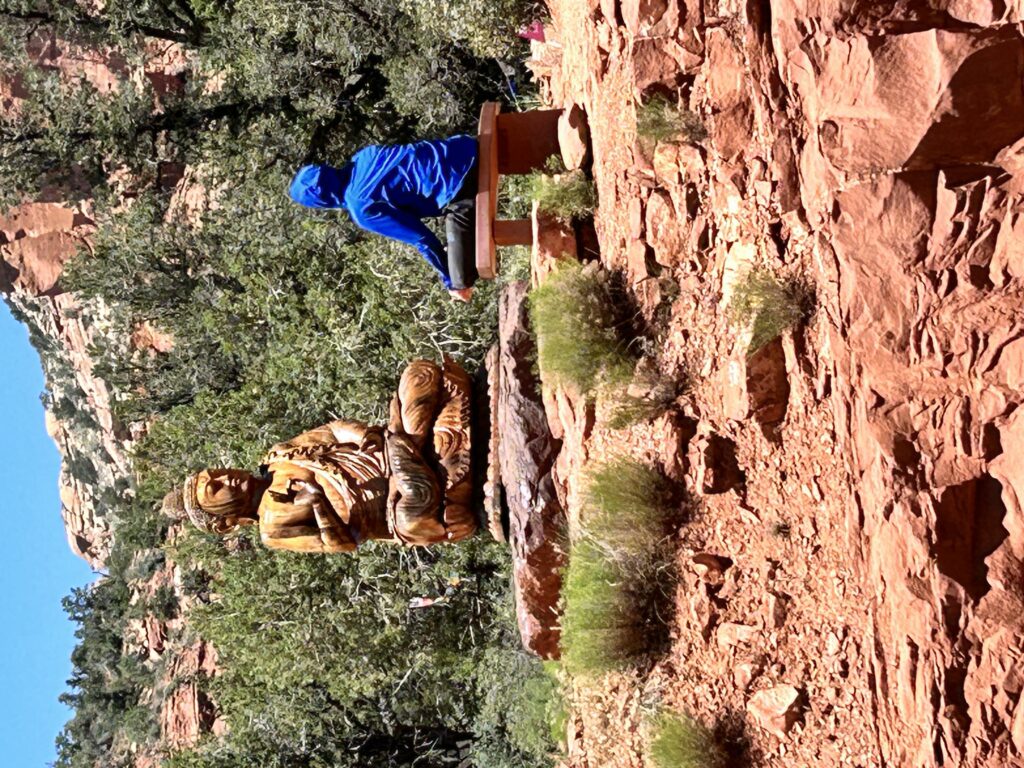 Young man in blue hoodie faces kneeling statue of the buddha: Sedona, AZ