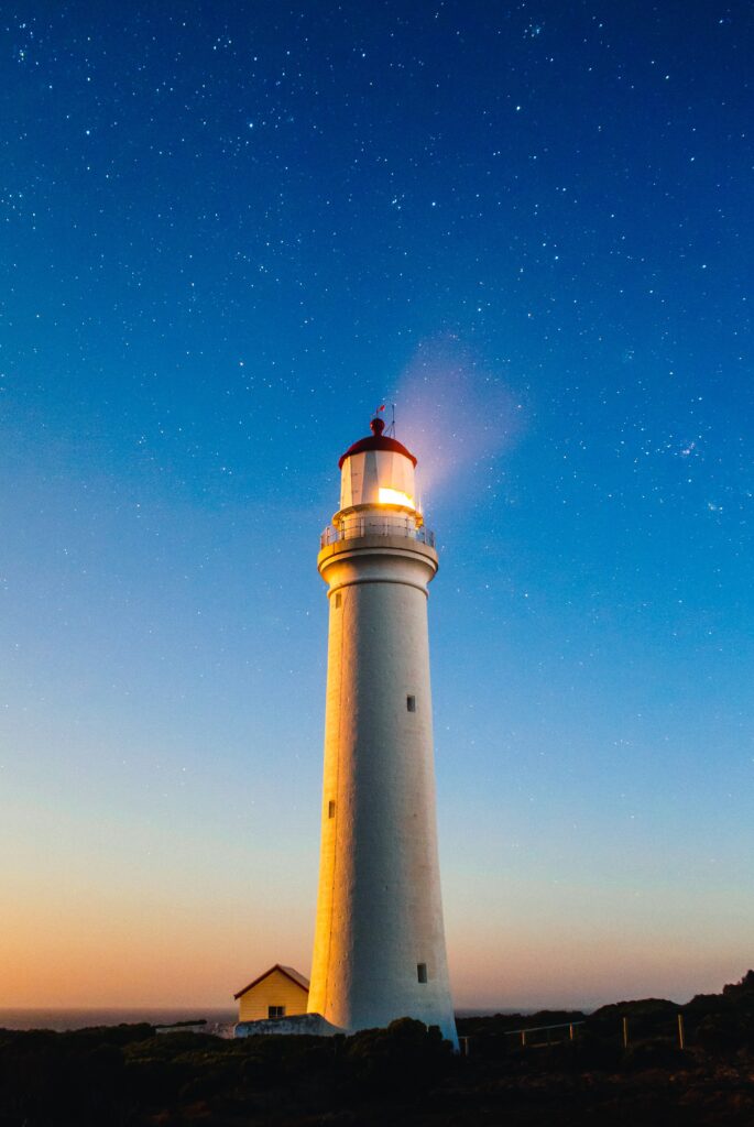 A lighthouse beaming light to a vaulted heaven of stars